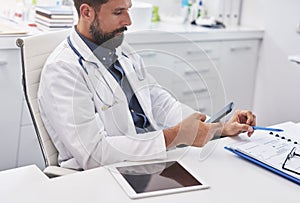 Male doctor using mobile phone in his doctorÃ¢â¬â¢s office photo
